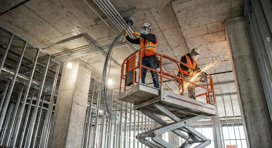 Electricians installing conduit using lift at construction site