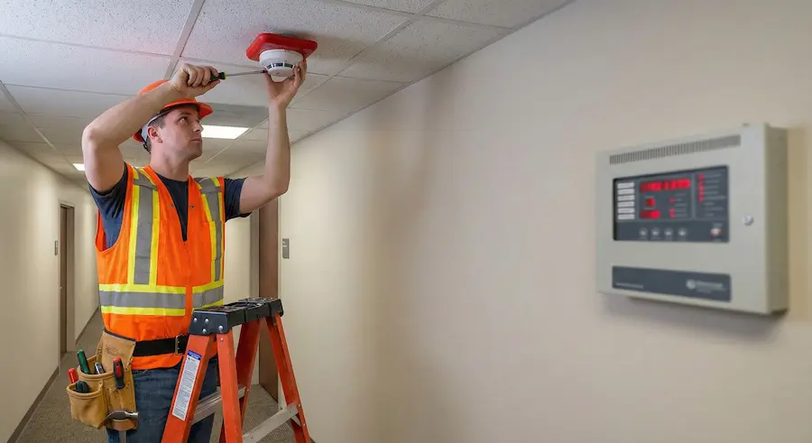 Electrician installing smoke detector in hallway